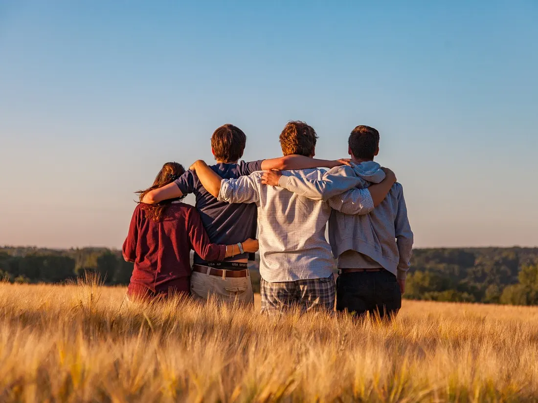 Four friends stand arm in arm in the evening light, looking out over a field.