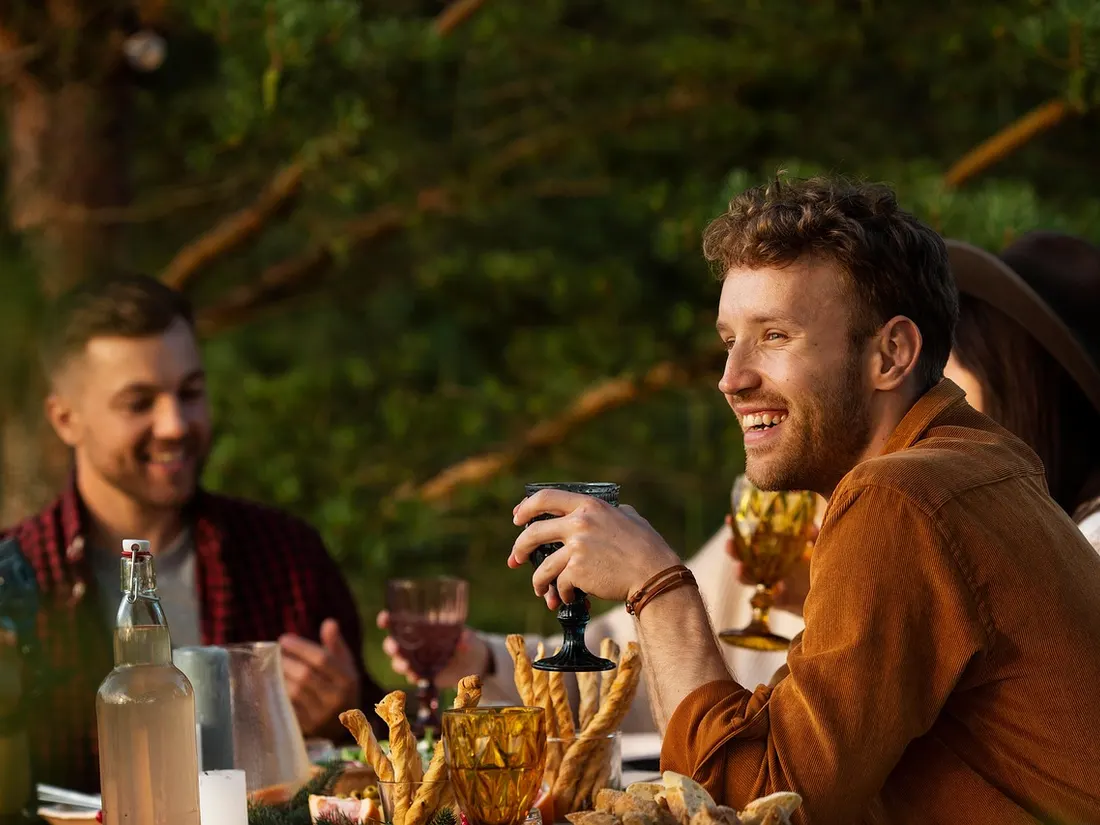 Friends laugh at a laid table outdoors in golden evening light.