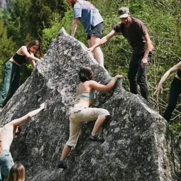 Friends bouldering on a big rock in a forest, helping each other up.